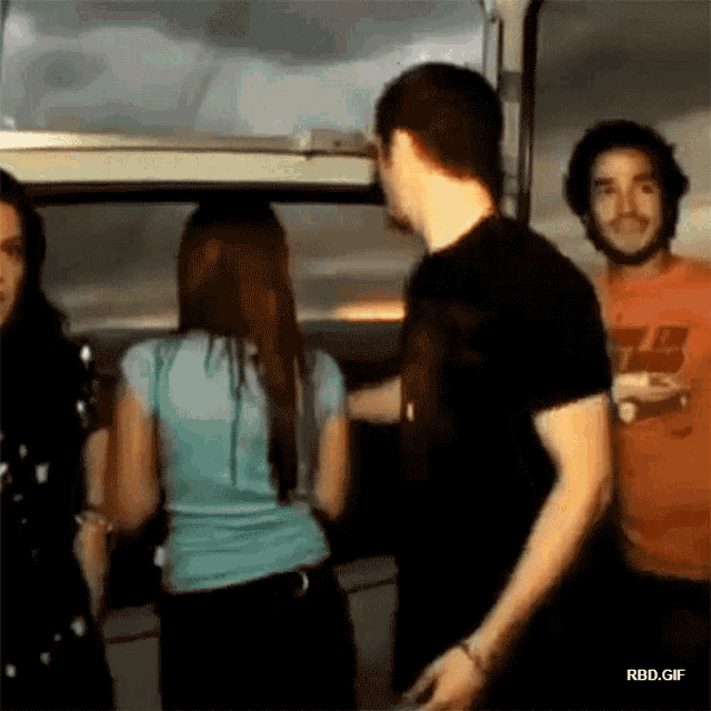 a group of people are standing in a room with a man wearing an orange shirt that says ' rbd.gif '