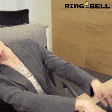 a man in a suit sits at a desk with a ring the bell logo behind him