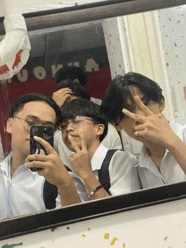 a group of boys are taking a picture of themselves in a mirror with a sign on the wall that says uoka