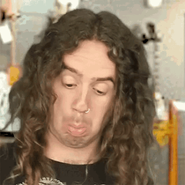 a man with long curly hair and a nose ring making a funny face