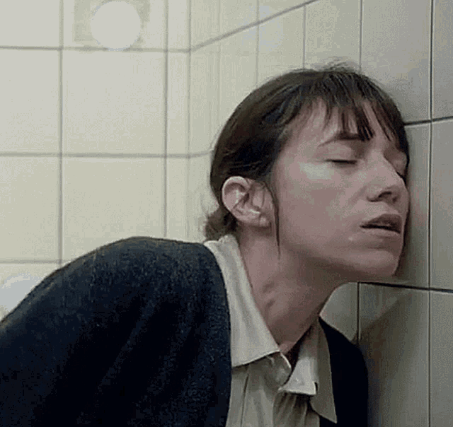 a woman is leaning against a tiled wall in a bathroom .