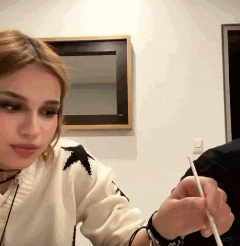 a woman is sitting at a table while a man is holding a chopstick .