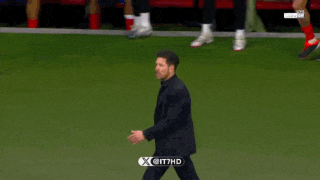 a man in a suit is walking on a soccer field with a x on it