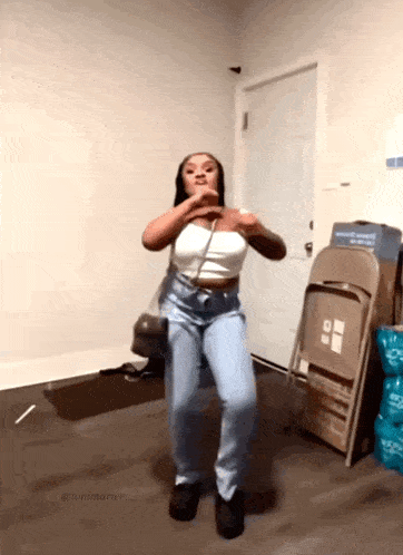 a woman in a white top and blue jeans is dancing in front of a folding chair