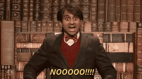 a man in a suit and bow tie is standing in front of a wall of books and making a funny face .