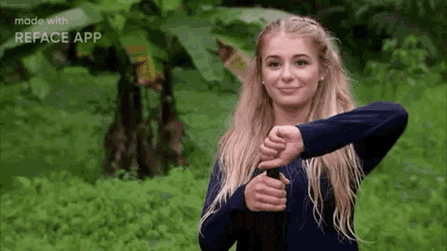 a young woman is giving a thumbs down sign while standing in the woods .