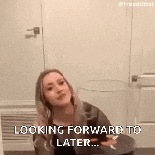 a woman is sitting on a toilet in a bathroom and looking forward to later .