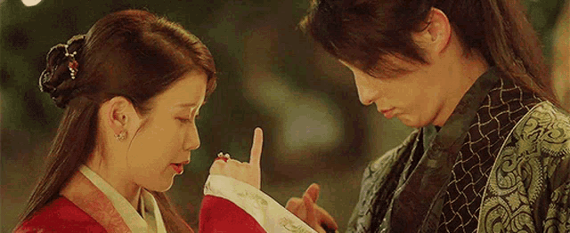 a man and a woman are standing next to each other and the woman is pointing to the man 's finger .