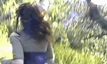 a woman is standing in the grass with her hair blowing in the wind .