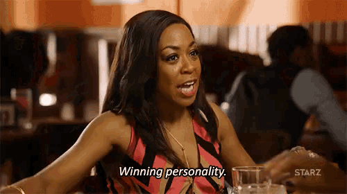 a woman is sitting at a table with a glass of wine and saying `` winning personality . ''