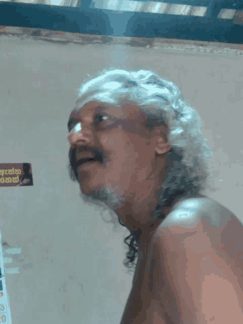 a man with gray hair and a mustache is standing in front of a wall with a sign that says ' a '