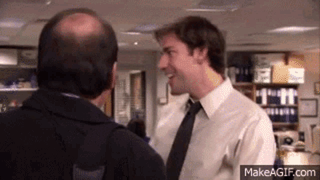 a man in a white shirt and black tie talking to another man