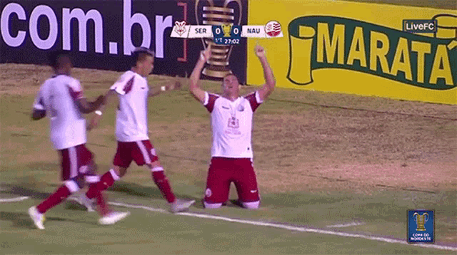 a group of soccer players celebrate a goal in front of a marata ad