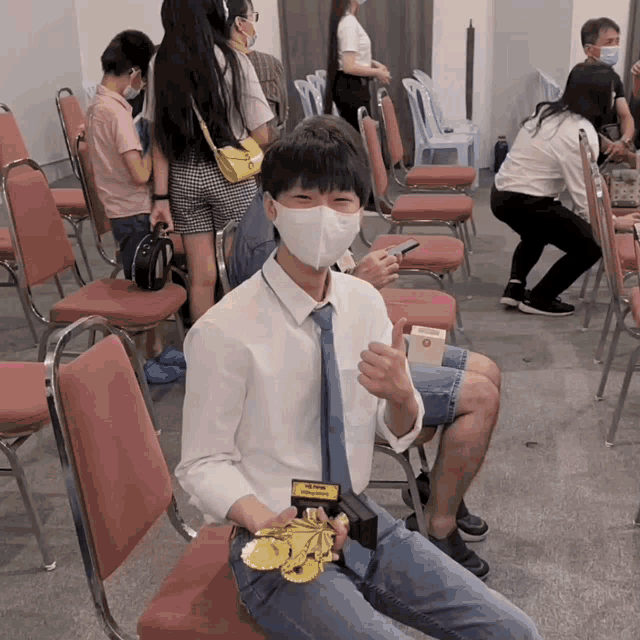 a man wearing a face mask sits in a chair holding a yellow item that says ' a ' on it