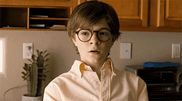 a young boy wearing glasses and a yellow shirt looks surprised