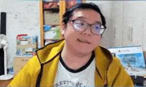 a man wearing glasses and a yellow jacket is sitting in front of a computer monitor .