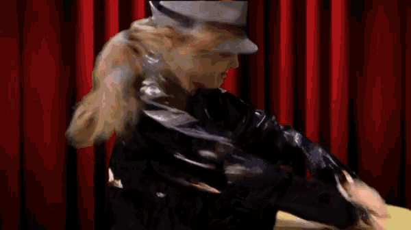 a woman in a hat and a black jacket stands in front of a red curtain