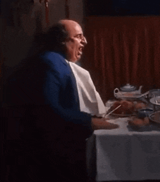 a bald man in a blue suit and tie is sitting at a table with a plate of food .