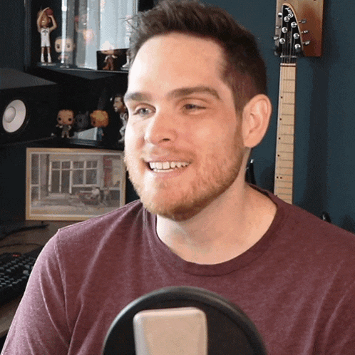 a man in a maroon shirt is smiling in front of a microphone