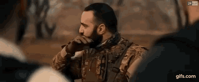 a man in a military uniform with a beard is talking on a cell phone in a crowd of people .