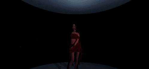 a woman in a red dress is standing on a stage with a red ribbon behind her