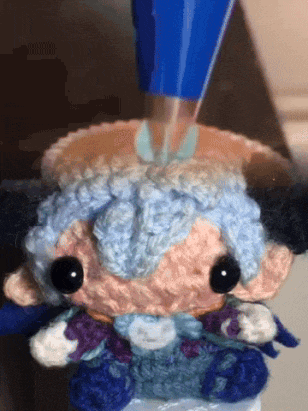 a close up of a crocheted stuffed animal with blue hair and black eyes