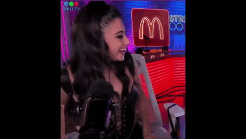 a woman is sitting in a chair with her hand in her hair and a neon sign in the background .