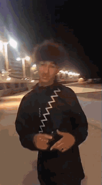 a man wearing a black jacket with a white stripe on the shoulder is standing in front of a building at night .