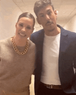 a man and a woman are posing for a picture together . the woman is wearing a gold chain necklace .