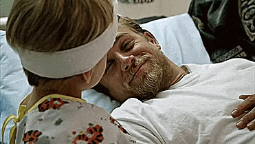 a little girl is kissing a bearded man in a hospital bed .
