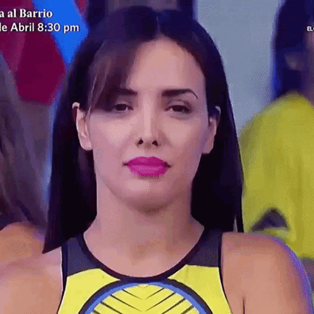 a woman wearing a yellow tank top and pink lipstick is standing in a crowd .