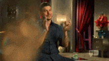a man in a blue shirt is sitting on a couch in a living room with his hands in the air .