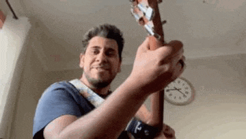 a man is playing a guitar in front of a clock .