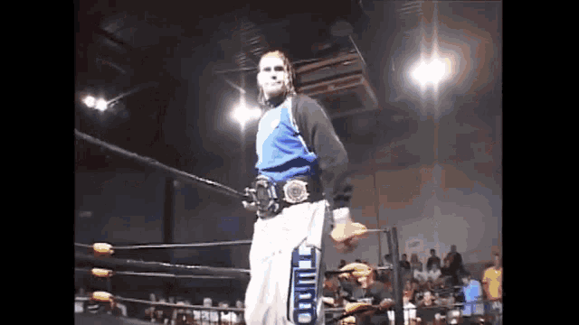 a wrestler is standing in a wrestling ring wearing a belt that says t on it .