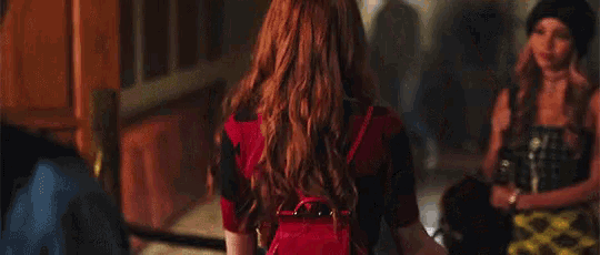 two women are holding hands in a hallway and one is wearing a plaid skirt