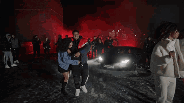 a man is carrying a woman in front of a car that has a license plate that says lpvj4