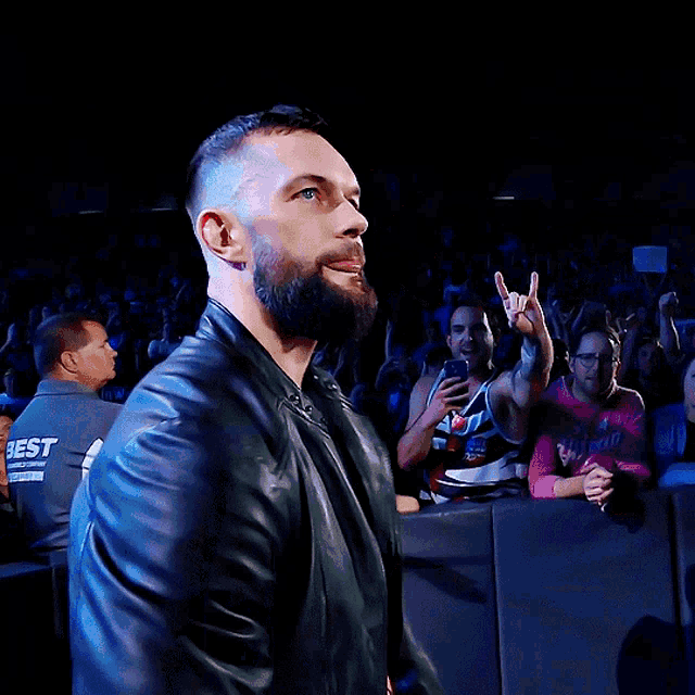 a man with a beard wears a black leather jacket with a red x on the front