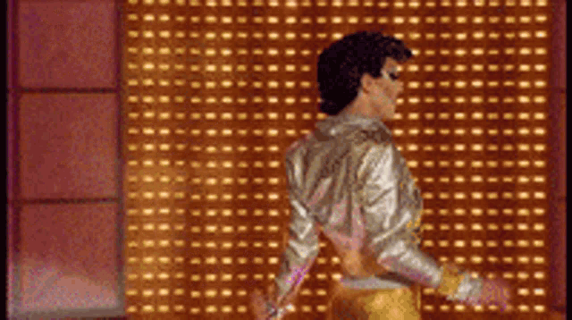 a man in a gold jacket is dancing in front of a wall with dots on it