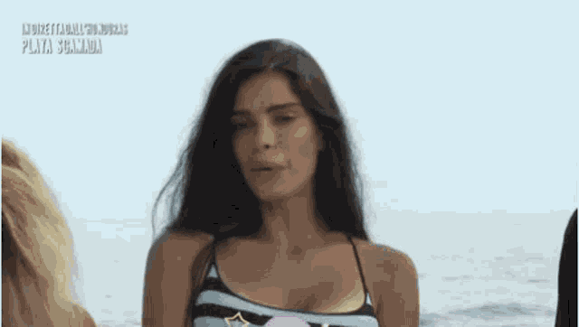 a woman in a striped bikini is standing on a beach in front of the ocean