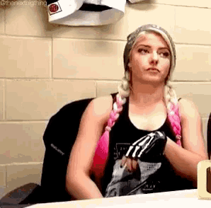a woman is sitting at a table in front of a brick wall wearing a tank top and gloves .