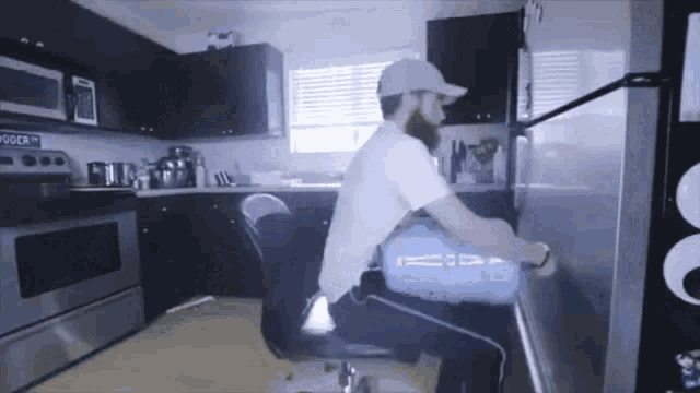 a man is sitting in a chair in front of a refrigerator in a kitchen with a sign that says " goodr "
