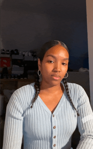 a woman wearing a light blue sweater and earrings looks at the camera
