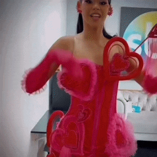 a woman in a red dress and pink gloves is holding a heart shaped object .