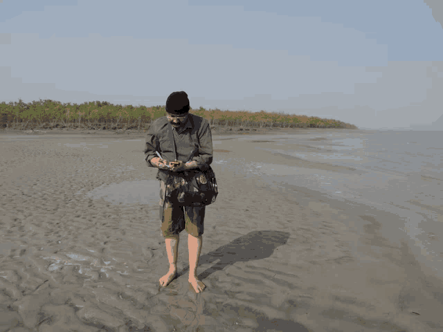 a man standing on a sandy beach looking at his cell phone