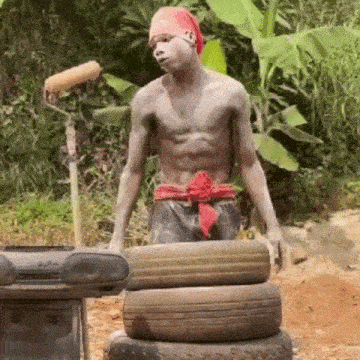 a shirtless man in a red bandana is standing on a pile of tires .