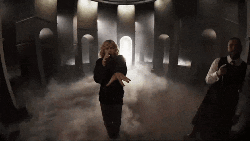 a woman is singing into a microphone in a dark room with smoke coming out of the ceiling .