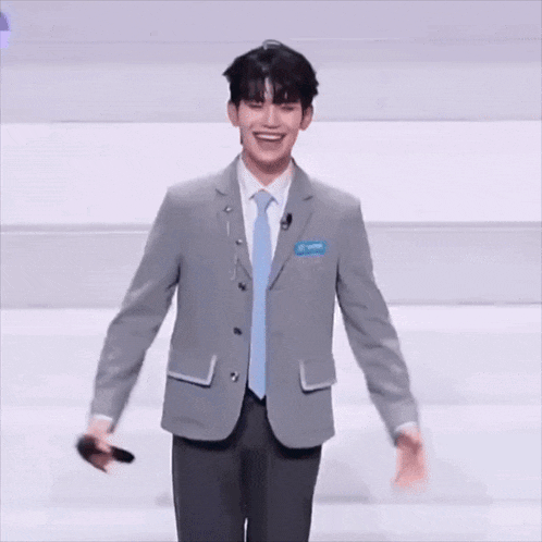 a man in a suit and tie is standing with his arms outstretched in front of a sign that says " ha "
