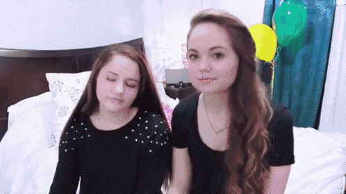 two girls are standing next to each other on a bed with balloons in the background