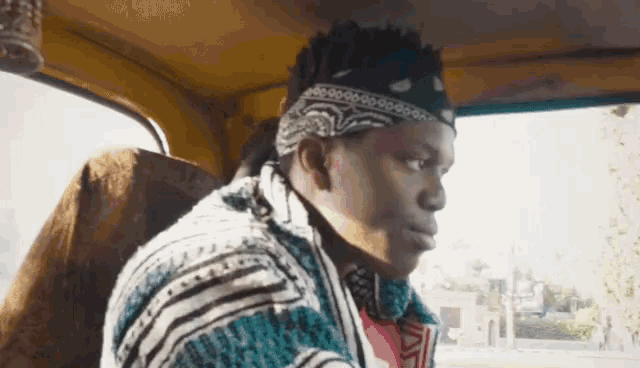 a man wearing a bandana and a striped shirt is sitting in the back seat of a car