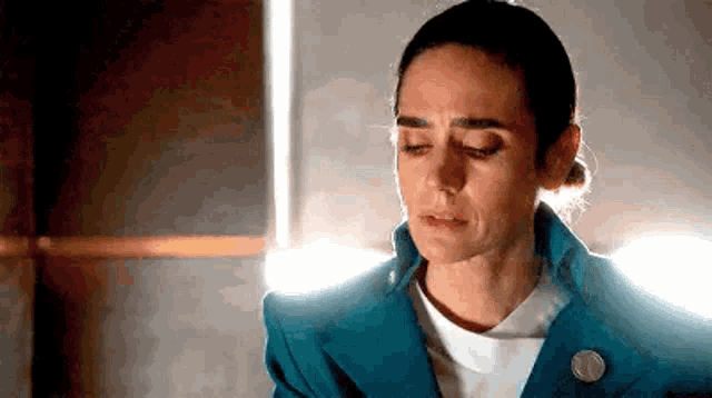 a woman in a blue jacket and white shirt is crying while sitting in front of a window .